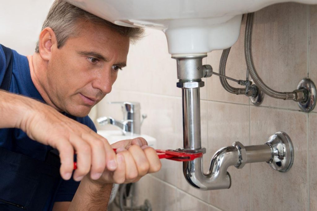 Un homme plombier est en train de serrer une canalisation dans une salle de bain